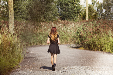 Rear view of woman walking on road by field - CAVF01216