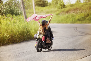 Frau hält einen Schal hoch, während sie mit einem Mann auf einem Motorrad sitzt - CAVF01235