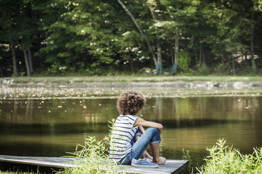 Rückansicht eines jugendlichen Mädchens, das auf einem Steg am See sitzt - CAVF01248