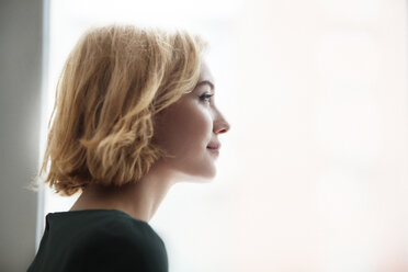 Close-up of happy woman by window at home - CAVF01262