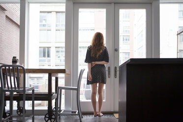 Woman looking through window at home - CAVF01271