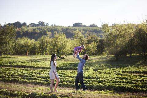 Mann hebt seine Tochter hoch, während er mit seiner Frau auf dem Feld steht, lizenzfreies Stockfoto