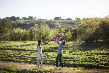 Mann hebt seine Tochter hoch, während er mit seiner Frau auf dem Feld steht - CAVF01290