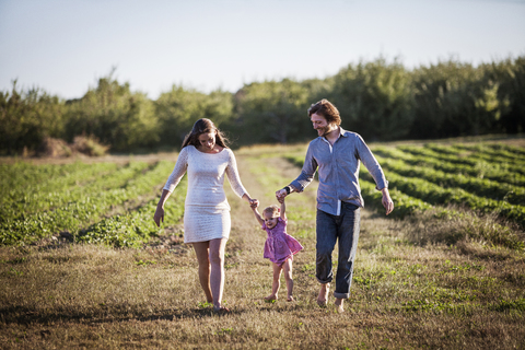 Glückliche Familie, die auf einem Feld in einem Bauernhof gegen den Himmel läuft, lizenzfreies Stockfoto