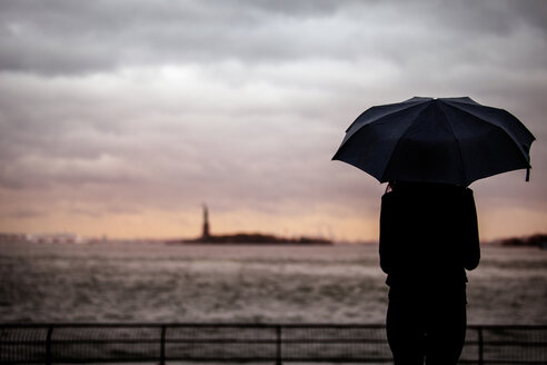 Rückansicht einer Frau mit Regenschirm, die vor einem bewölkten Himmel steht - CAVF01334