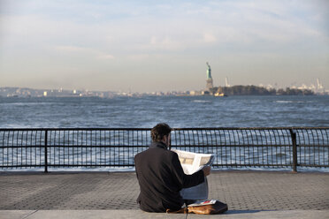 Mann liest Zeitung, während er auf der Promenade am Hudson River sitzt - CAVF01342