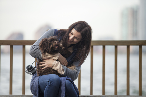 Frau sieht Hund an, während sie auf einer Bank am Hudson River sitzt, lizenzfreies Stockfoto