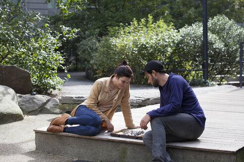 Paar spielt Schach, während es auf einer Bodenplatte im Rasen sitzt - CAVF01353