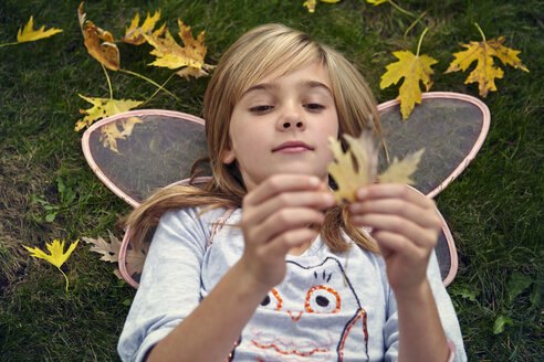 High angle view of girl in fairy costume holding leave while ly8ing on filed - CAVF01355