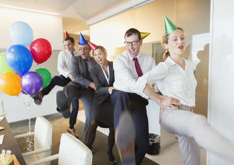 Playful business people with party hats dancing in conga line - CAIF06611