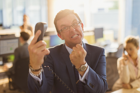 Furious businessman gesturing with fist at telephone in office stock photo