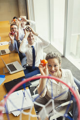 Business people aiming plastic balls at basketball hoop in conference room - CAIF06613