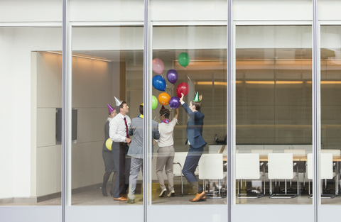 Playful business people in party hats celebrating with balloons in conference room stock photo