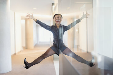 Symmetrische Reflexion Porträt der spielerischen Geschäftsfrau mit Armen und Beinen auseinander im Büro Korridor - CAIF06620