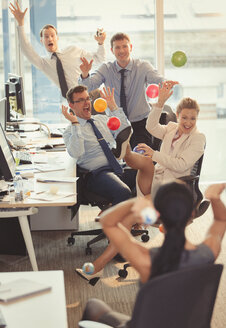 Playful business people throwing colorful plastic balls at each other in office - CAIF06627