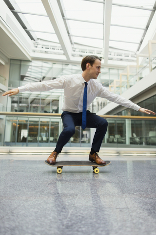Playful businessman skateboarding in office corridor stock photo