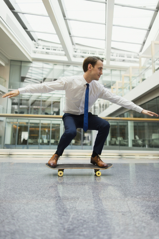 Verspielter Geschäftsmann auf dem Skateboard im Bürokorridor, lizenzfreies Stockfoto