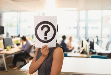 Portrait of businesswoman holding question mark printout over her face in office - CAIF06631