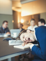 Tired businessman yawning and laying on conference table - CAIF06646