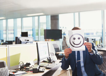 Porträt eines Geschäftsmannes, der einen Smiley-Ausdruck über sein Gesicht im Büro hält - CAIF06656