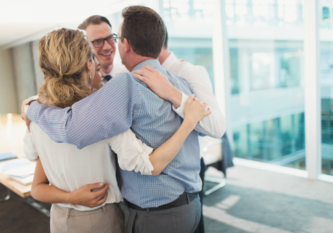 Smiling business people hugging in huddle in conference room stock photo