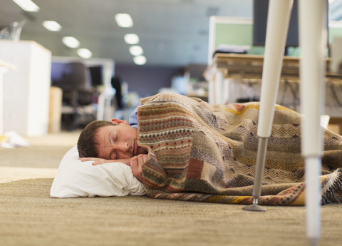 Geschäftsmann mit Kissen und Decke schlafend auf dem Büroboden, lizenzfreies Stockfoto