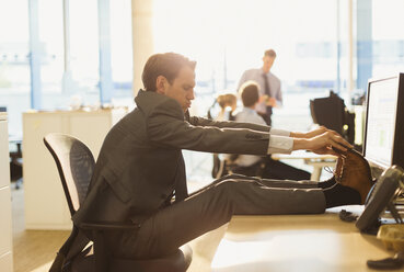 Businessman stretching feet on desk in office - CAIF06667