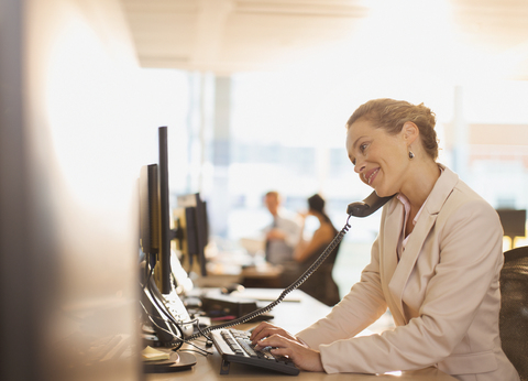 Lächelnde Geschäftsfrau, die am Telefon spricht und am Computer im Büro arbeitet, lizenzfreies Stockfoto