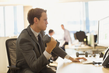 Businessman doing biceps curls with dumbbell at computer in office - CAIF06669