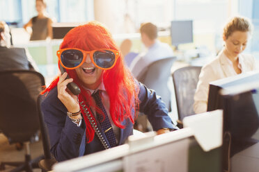 Porträt verspielter Geschäftsmann mit roter Perücke und großer Sonnenbrille im Büro - CAIF06671