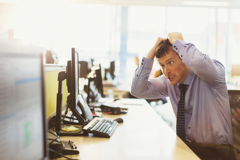 Gestresster Geschäftsmann, der sich am Computer im Büro die Haare rauft, lizenzfreies Stockfoto