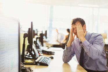 Stressed businessman with head in hands at office desk - CAIF06688