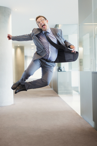 Überschwänglicher Geschäftsmann, der im Büroflur vor Freude springt, lizenzfreies Stockfoto
