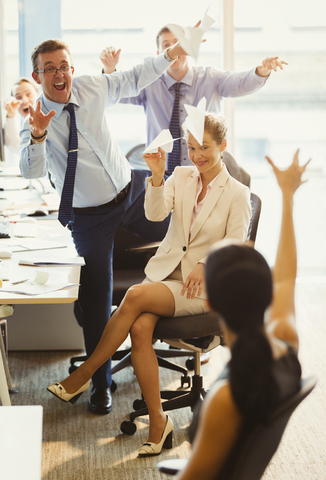 Playful business people throwing paper airplanes at each other in office stock photo