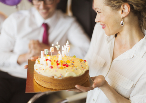 Smiling businesswoman holding birthday cake with candles stock photo