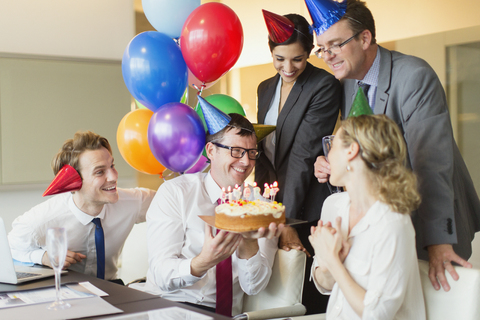 Colleagues presenting businesswoman with birthday cake in conference room stock photo