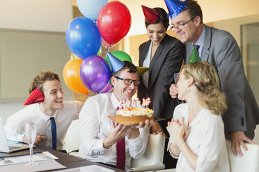 Colleagues presenting businesswoman with birthday cake in conference room - CAIF06715