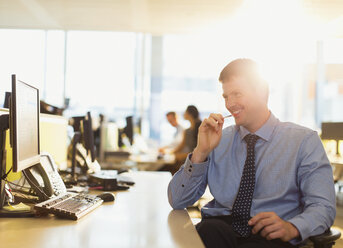 Lächelnder Geschäftsmann am Computer in einem sonnigen Büro - CAIF06724