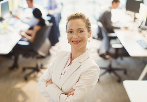 Porträt einer selbstbewussten Geschäftsfrau mit verschränkten Armen im Büro, lizenzfreies Stockfoto