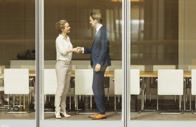 Businessman and businesswoman handshaking at conference room window - CAIF06727