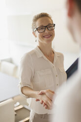 Smiling businesswoman shaking hands with businessman - CAIF06728