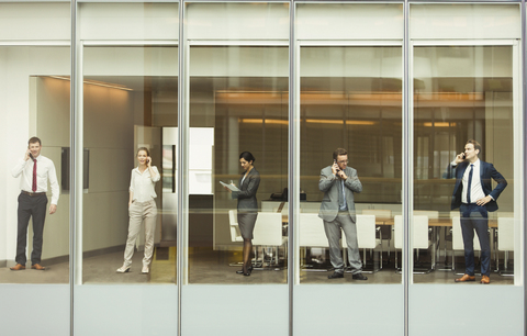 Geschäftsleute, die am Fenster des Konferenzraums mit Handys telefonieren und Papierkram durchgehen, lizenzfreies Stockfoto