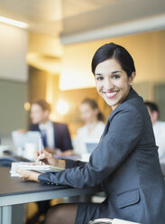 Porträt einer lächelnden Geschäftsfrau, die in einem Konferenzraum Notizen macht - CAIF06732