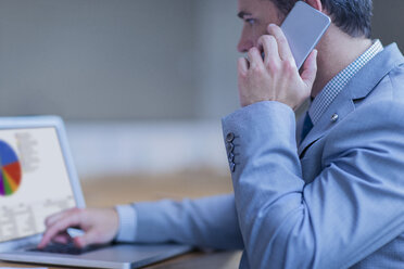 Geschäftsmann, der mit einem Handy telefoniert und an einem Laptop arbeitet - CAIF06743