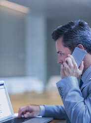 Businessman talking on cell phone and working at laptop in conference room - CAIF06749