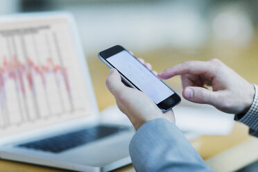 Close up of businessman dialing cell phone at laptop - CAIF06755