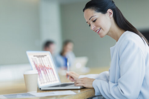 Lächelnde Geschäftsfrau bei der Arbeit am Laptop mit Kaffee im Konferenzraum - CAIF06756