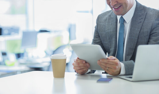 Lächelnder Geschäftsmann mit digitalem Tablet und Kaffee im Büro - CAIF06769