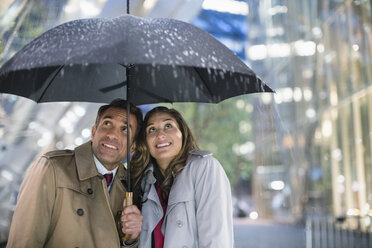 Geschäftsmann und Geschäftsfrau beobachten Regen unter Regenschirm - CAIF06776