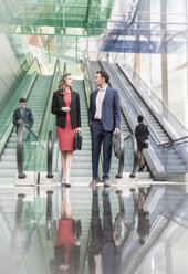 Geschäftsmann und Geschäftsfrau im Gespräch unter Rolltreppen in einer modernen Lobby - CAIF06787